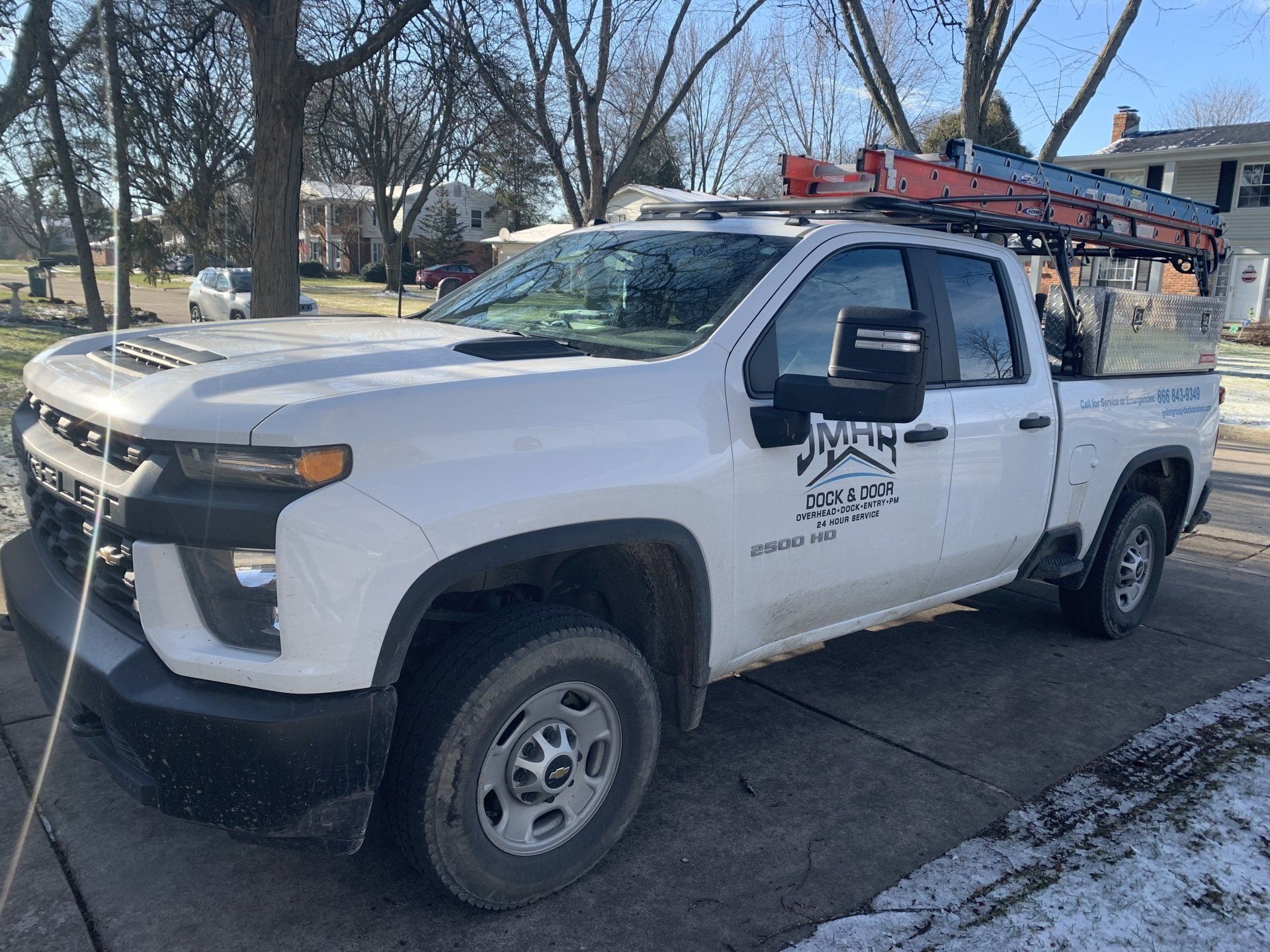 White work truck parked on a residential street; ladder on top.