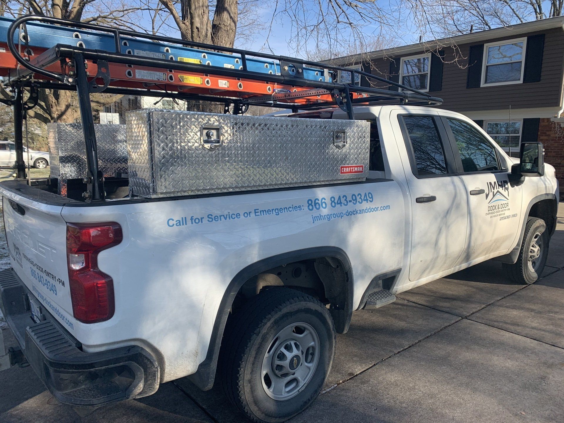White pickup truck with a ladder rack, toolbox, and ladder parked on a driveway.