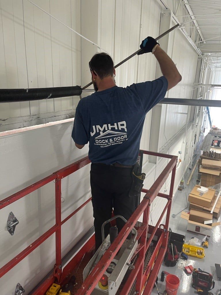 Person on lift installing something on a wall, in a large, bright room.