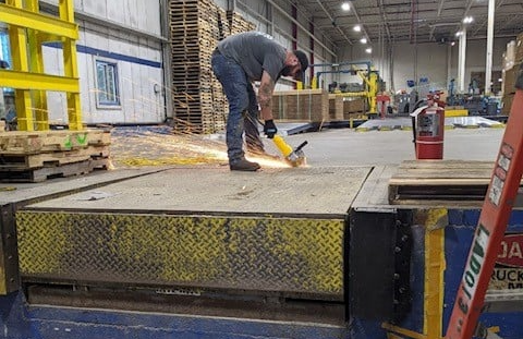 Man using an angle grinder on a metal dock. Sparks fly. Industrial setting.