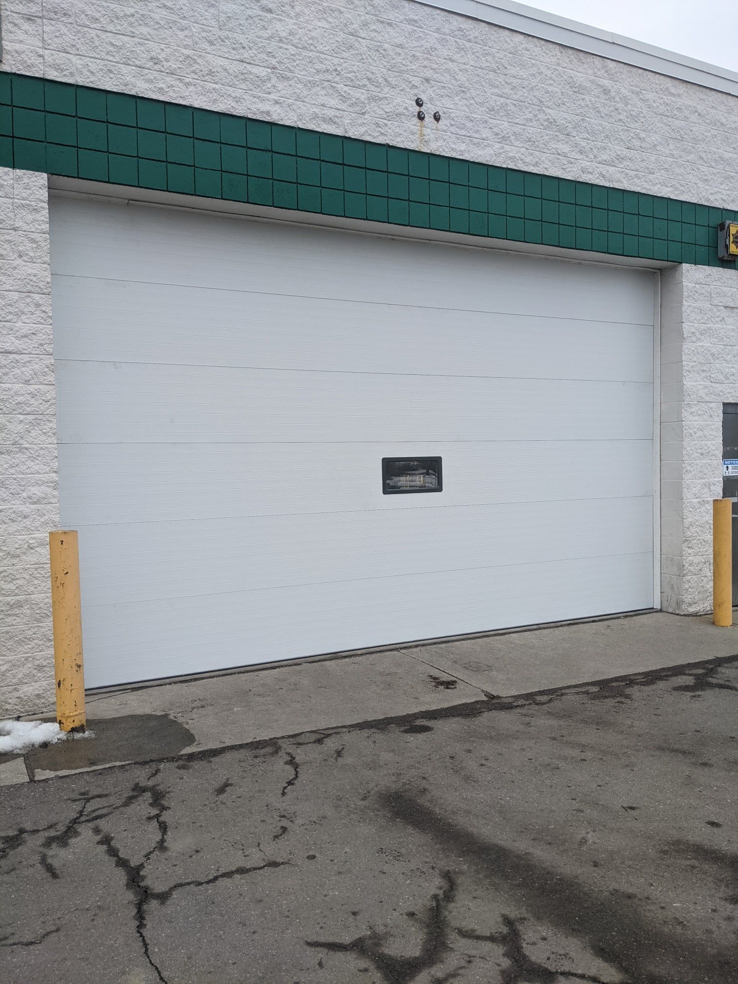 White garage door on a commercial building, with a dark handle, in an asphalt parking area.