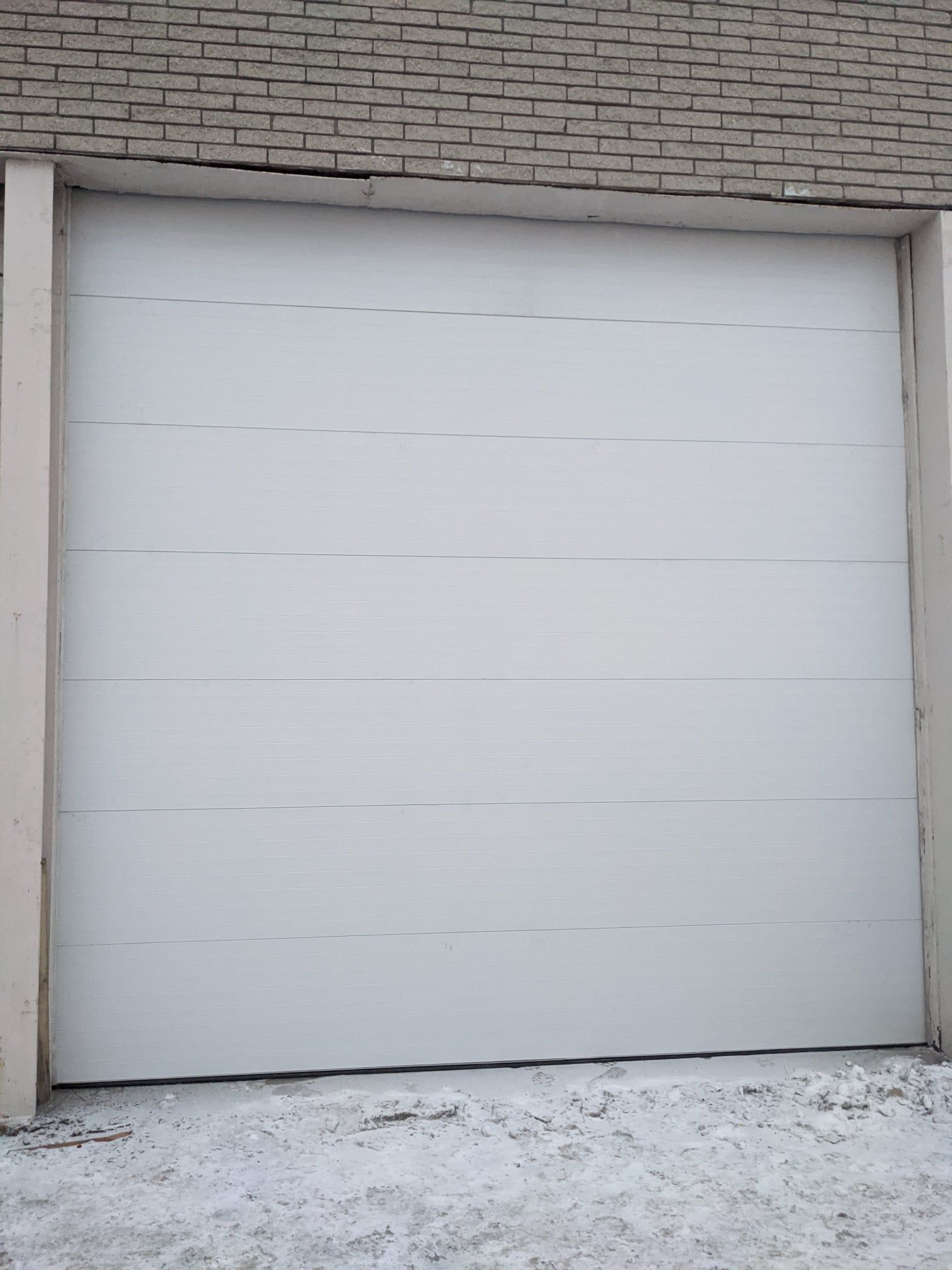 White garage door, framed by concrete columns, against a brick building background with snow.