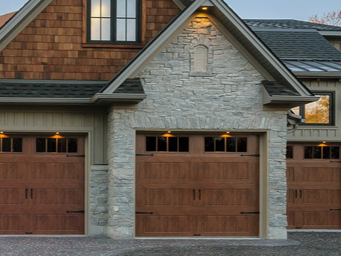 Three-car garage with brown doors, stone facade, and brown shingle siding on a house.