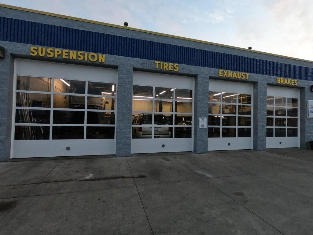 Exterior of a car repair shop with garage doors. Signs above doors say 