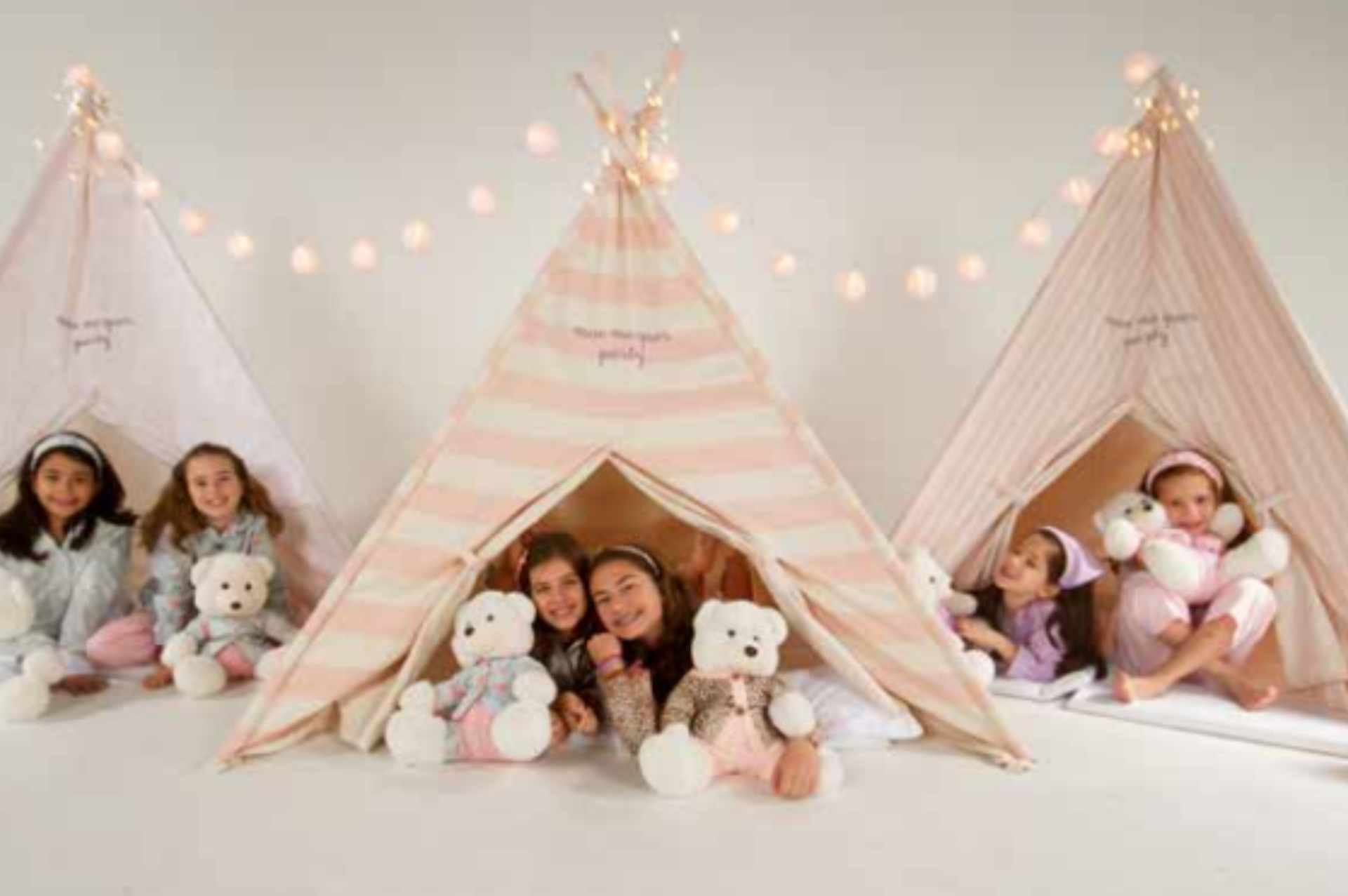 Um grupo de meninas estão sentadas em tendas com ursinhos de pelúcia.