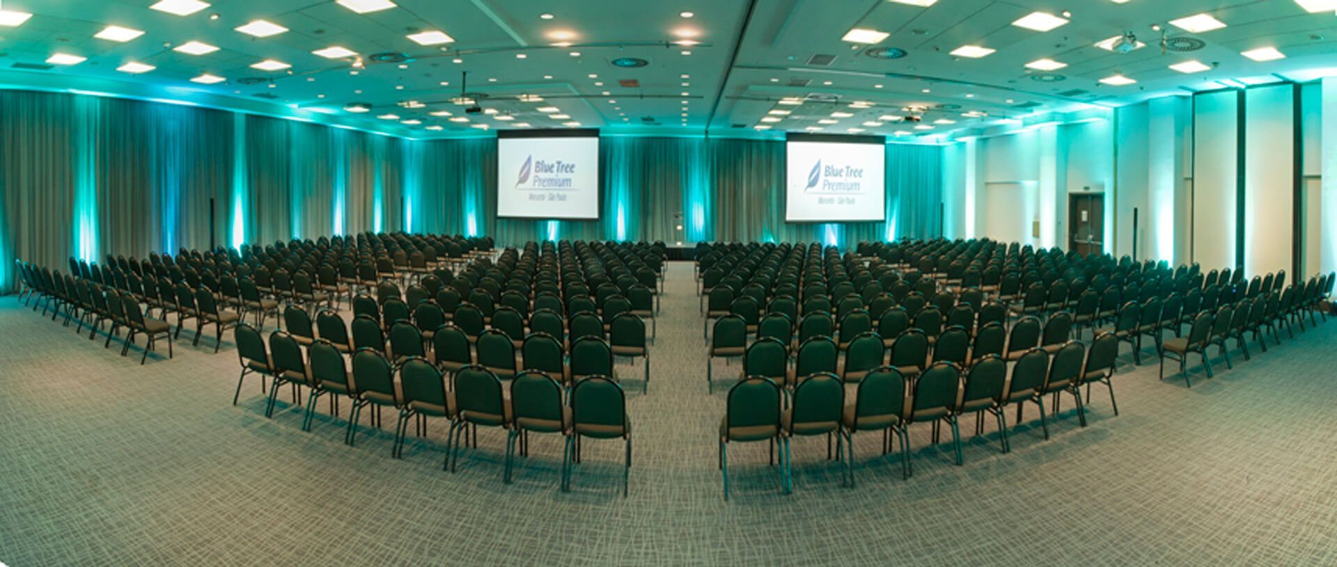 Uma grande sala de conferências com fileiras de cadeiras e duas telas