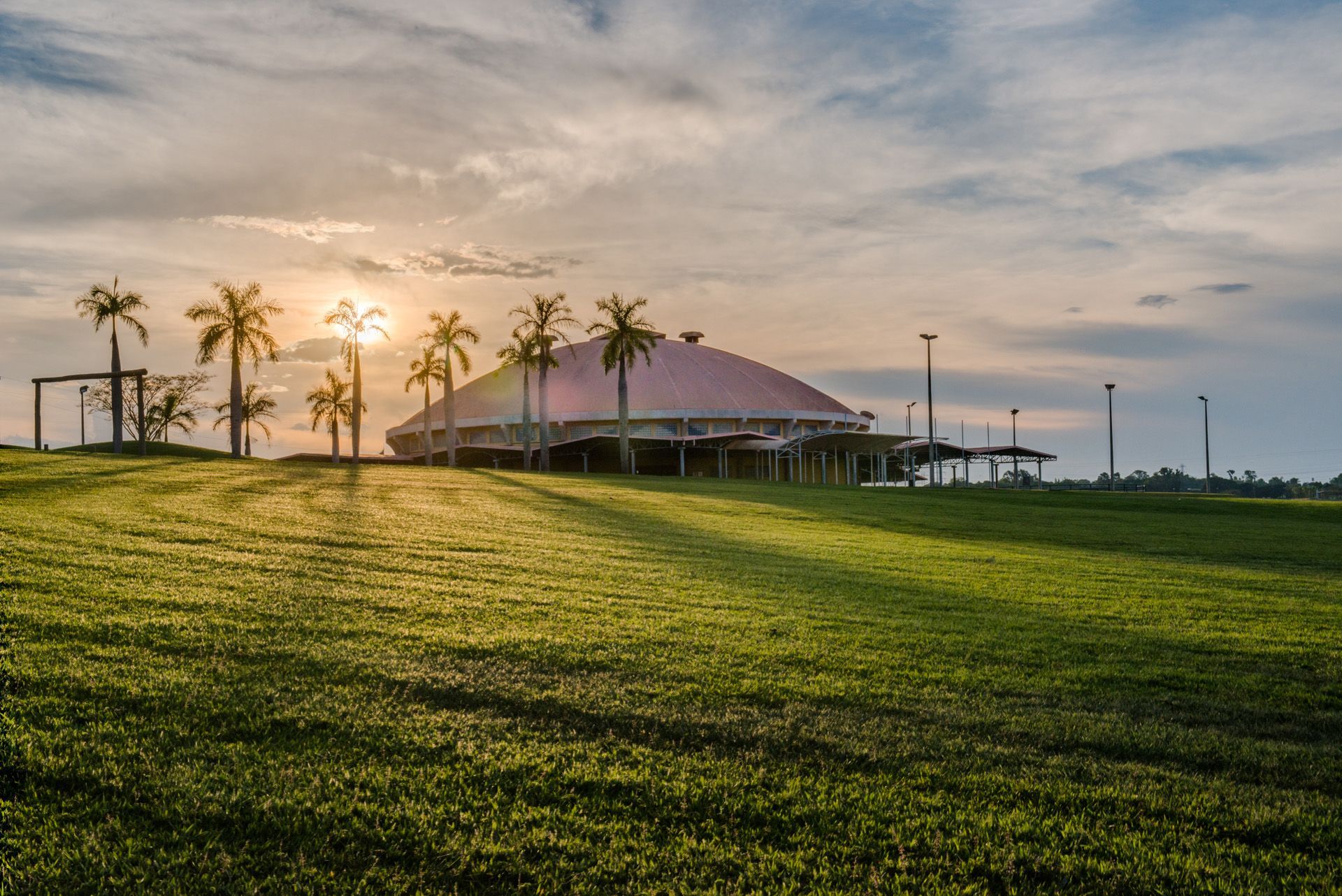 Um grande edifício com um telhado rosa é cercado por palmeiras em um campo gramado.