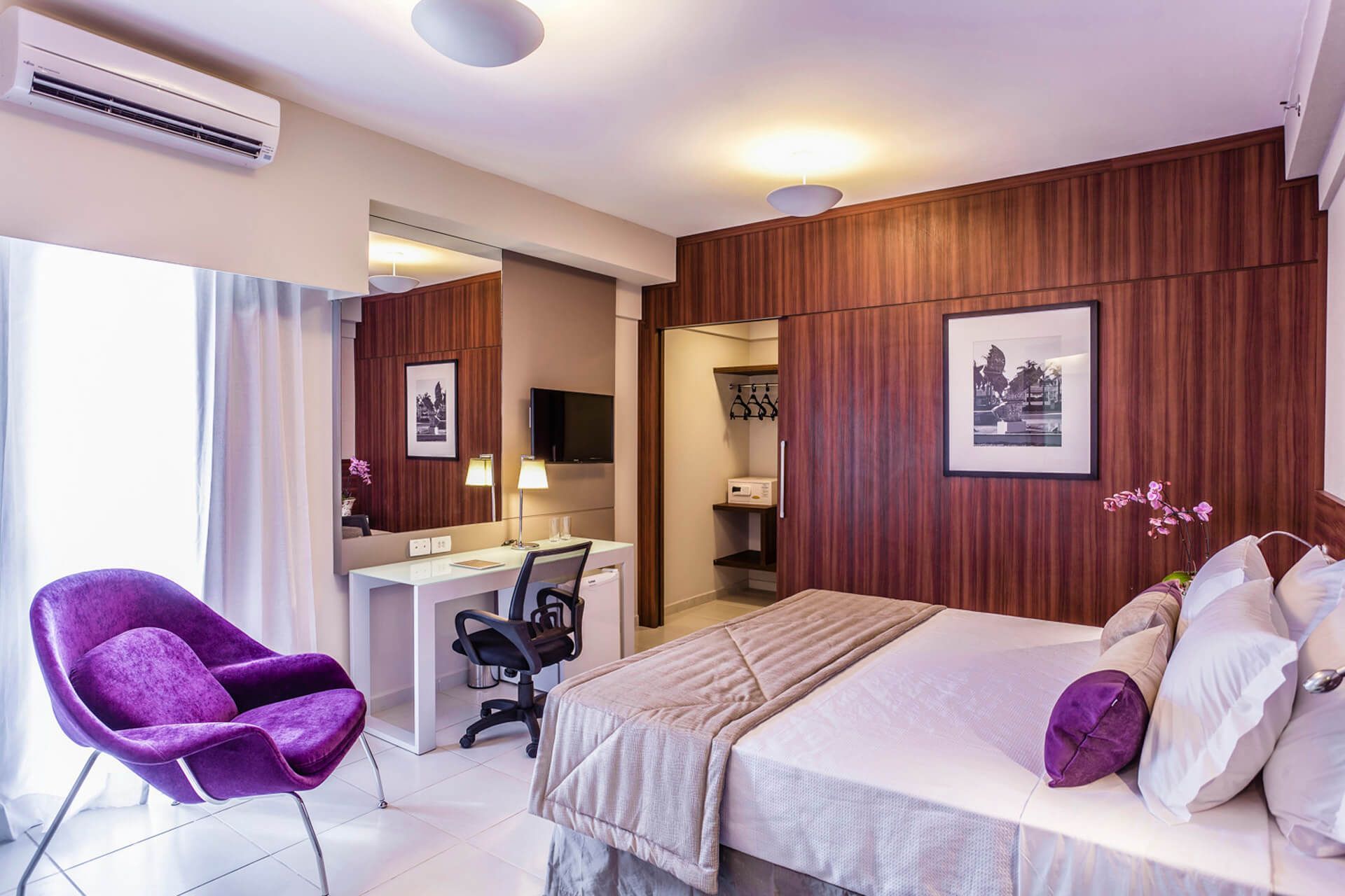 Um quarto de hotel com uma cama, cadeira, escrivaninha e espelho.