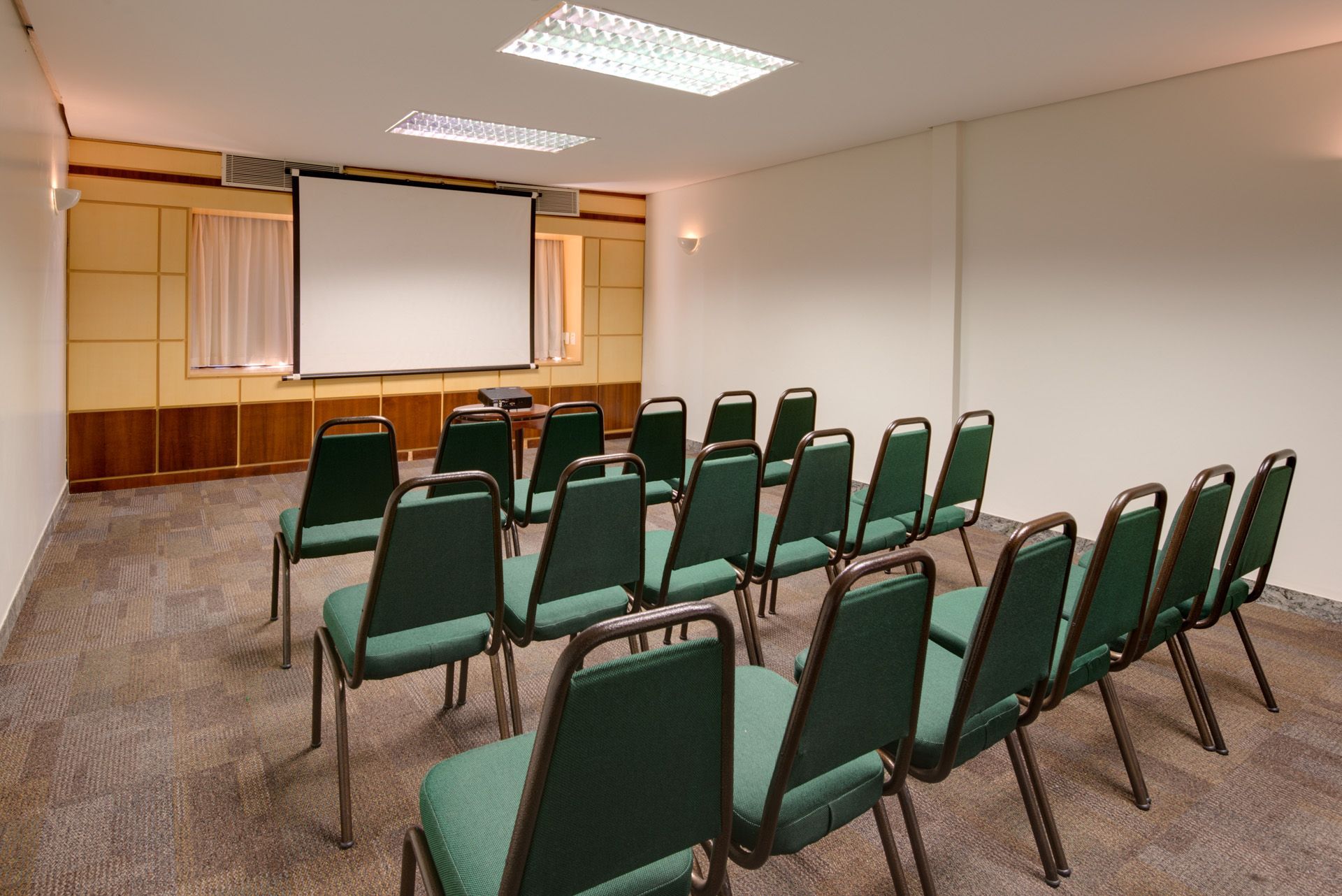 Uma sala de conferências com cadeiras verdes e uma tela de projetor