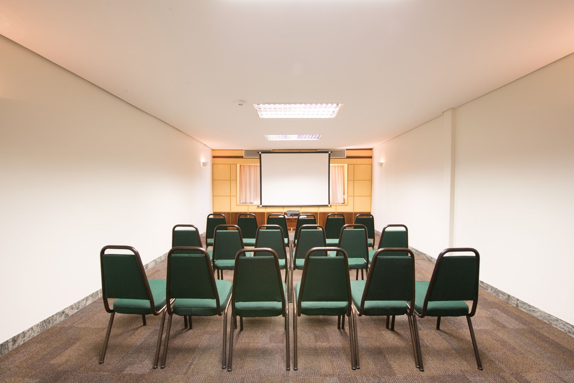 Uma sala de conferências com cadeiras verdes e uma tela de projetor