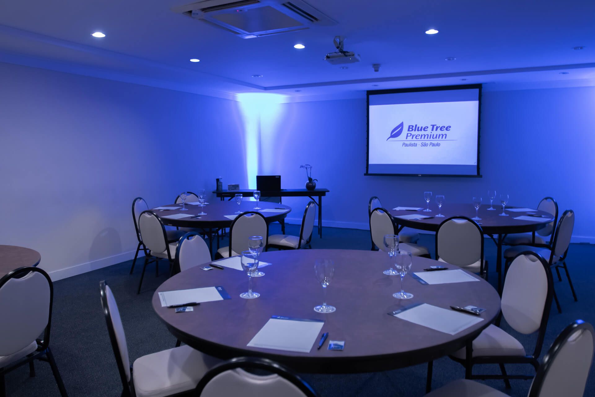 Uma sala de conferências com mesas e cadeiras e uma tela de projetor.