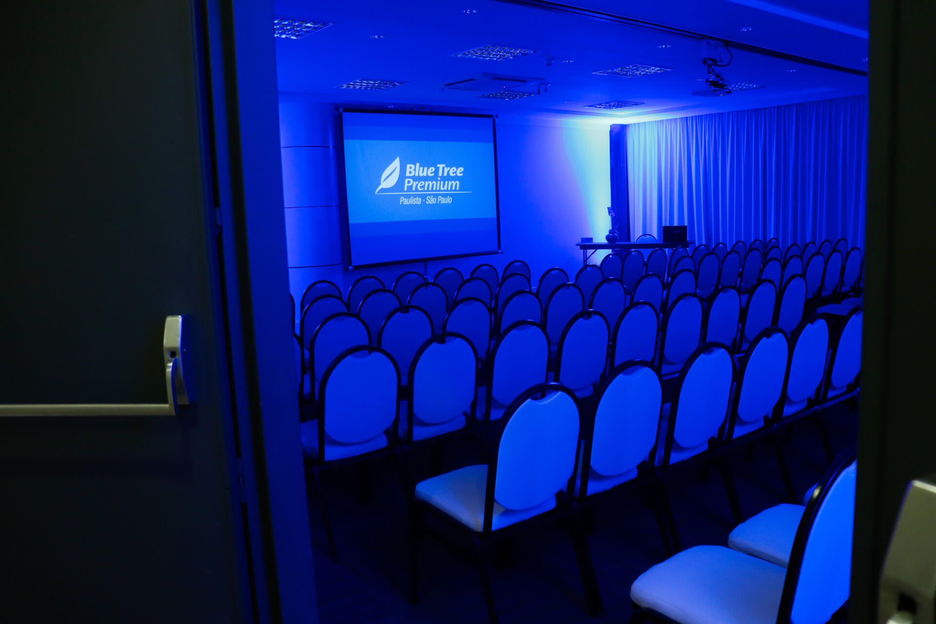 Uma sala de conferências com cadeiras azuis e uma tela de projetor