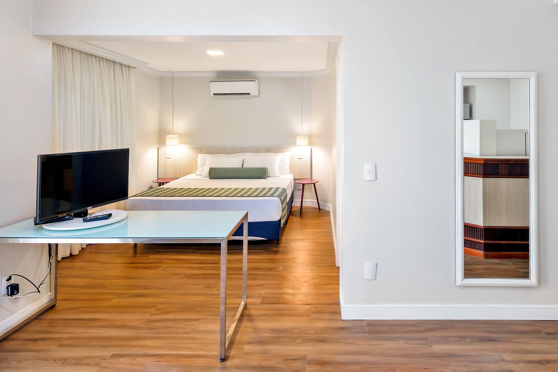 Um quarto de hotel com cama, escrivaninha, televisão e espelho.