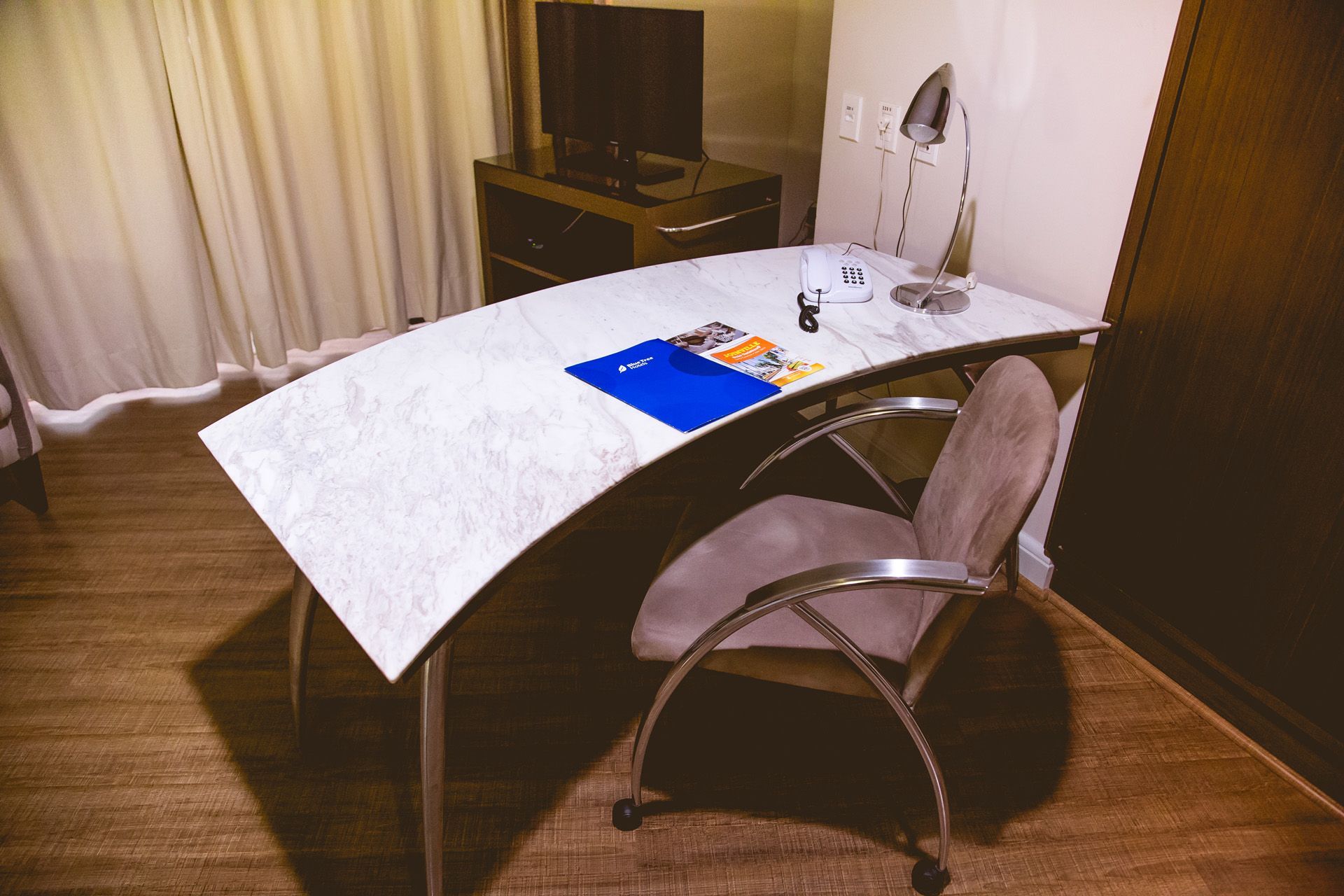 Uma mesa curva com uma cadeira em um quarto de hotel.