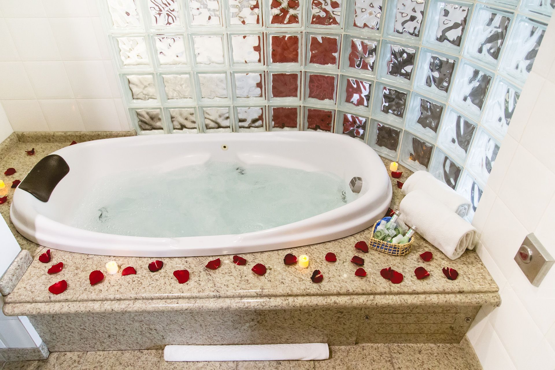 Um banheiro com banheira de hidromassagem cercada por pétalas de rosas e velas.