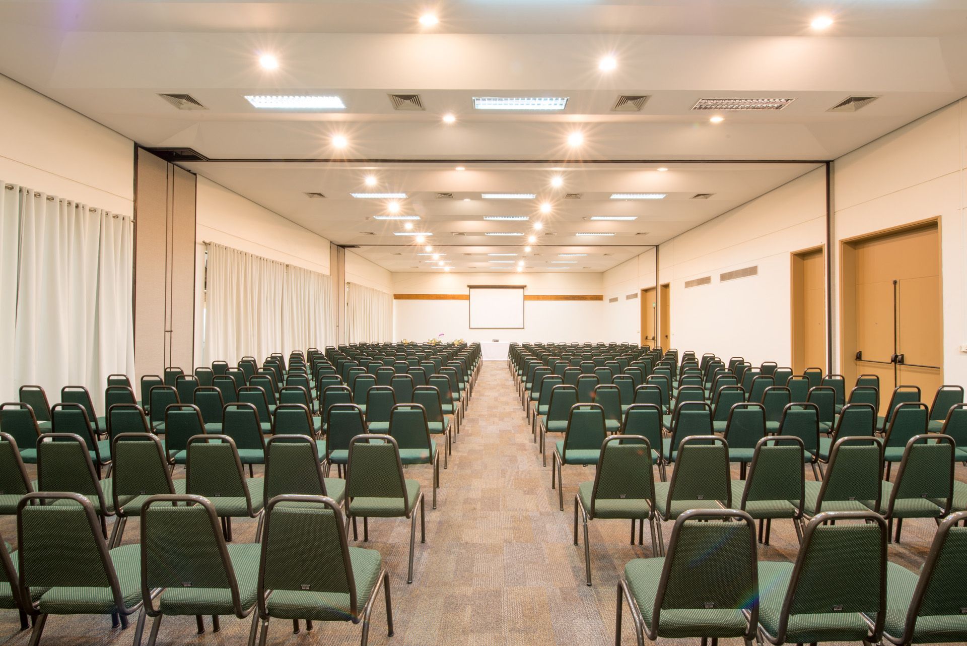 Uma grande sala cheia de fileiras de cadeiras e uma tela de projetor.