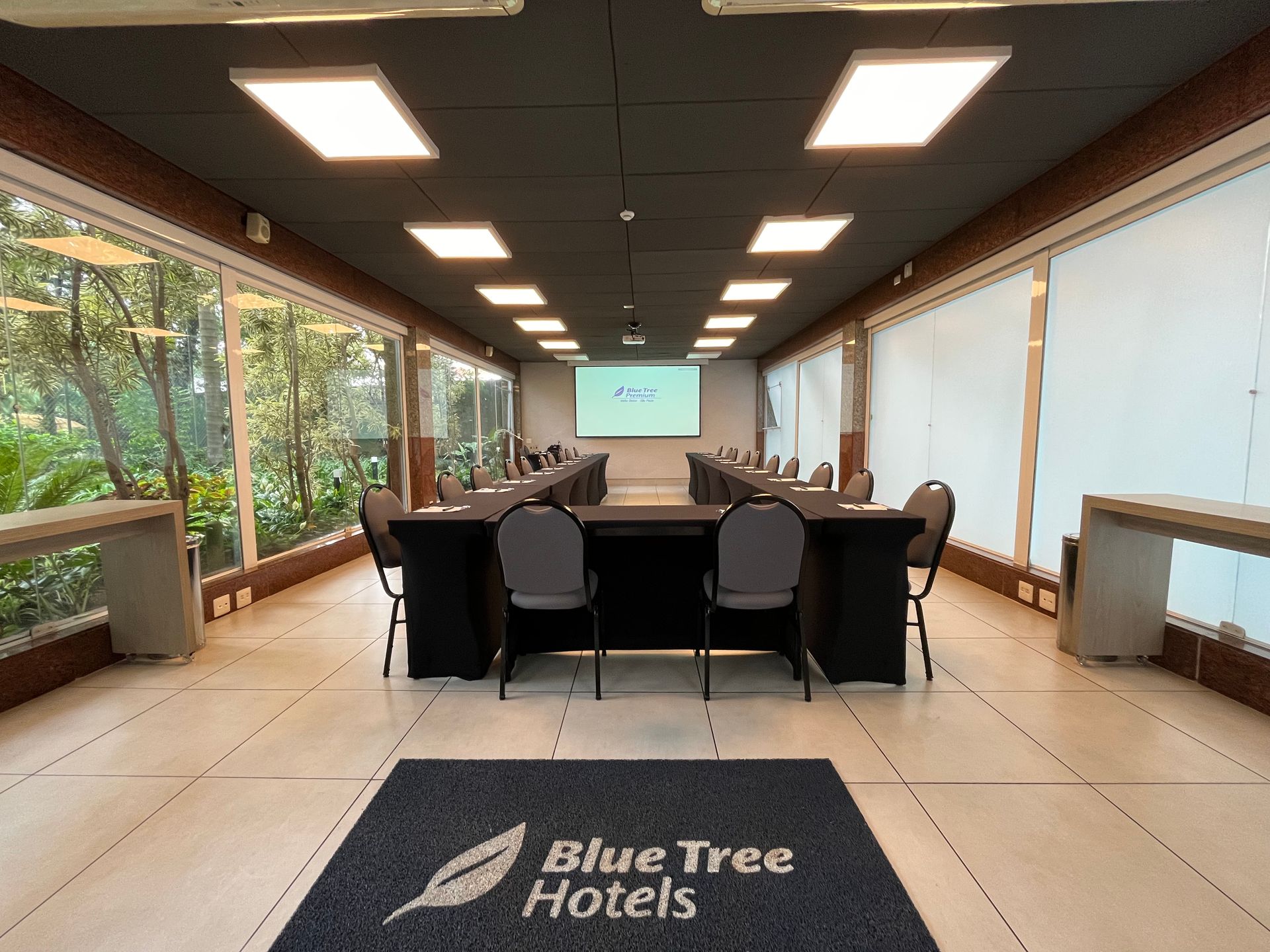 Uma grande sala de conferências com mesas e cadeiras e um logotipo de hotel em forma de árvore azul no chão.