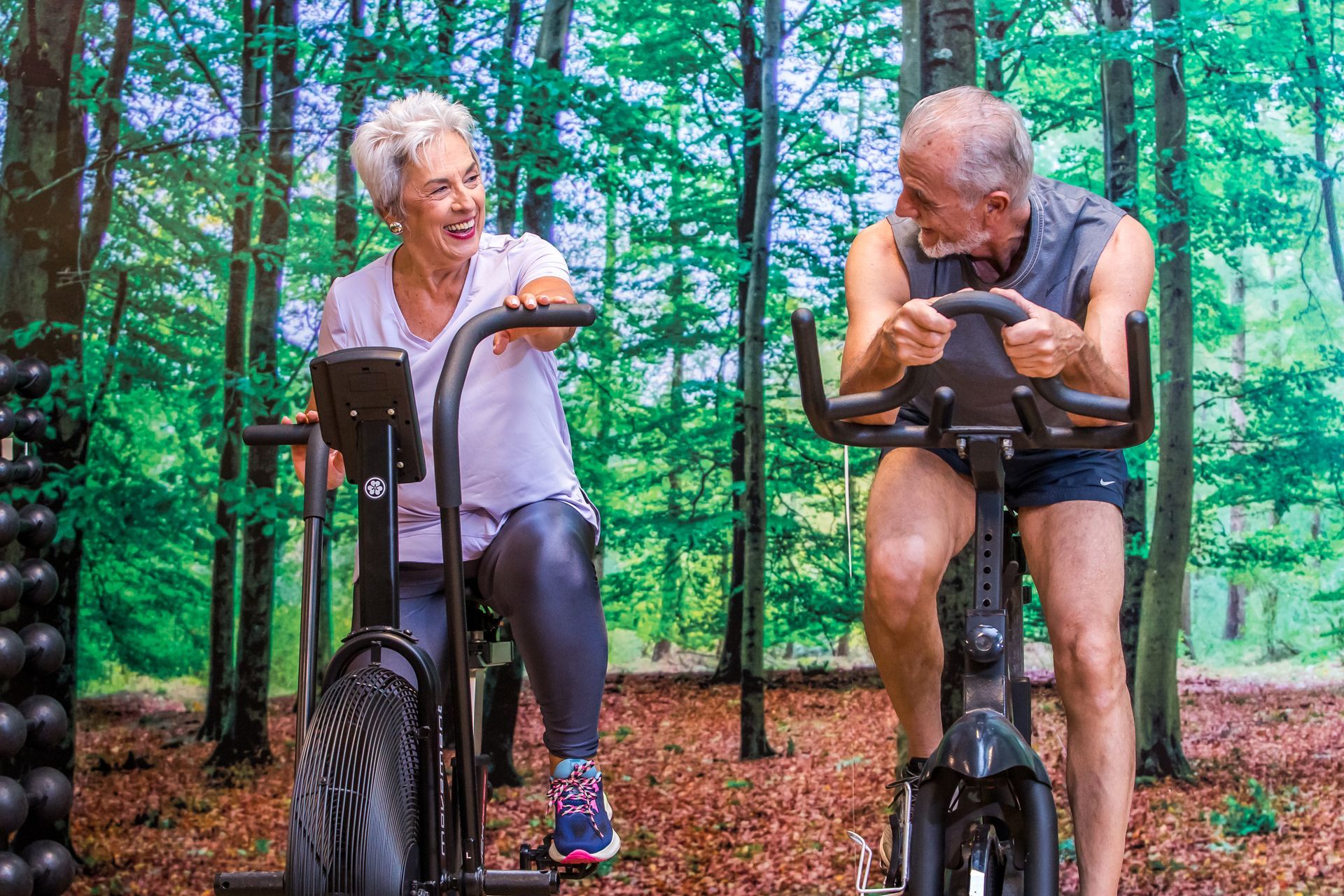 Um homem e uma mulher estão andando de bicicleta ergométrica na floresta.