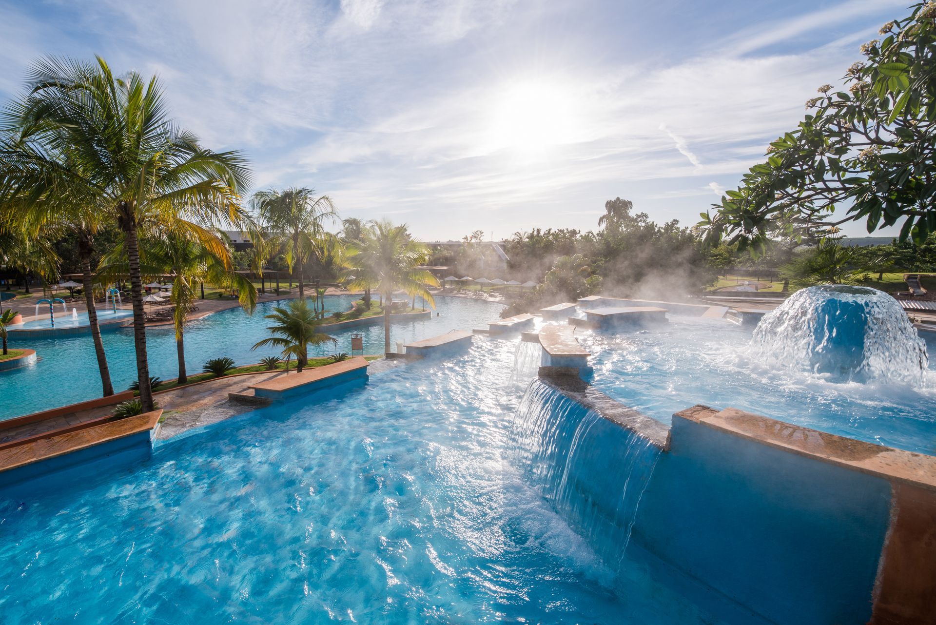 Uma grande piscina rodeada por palmeiras e uma fonte.