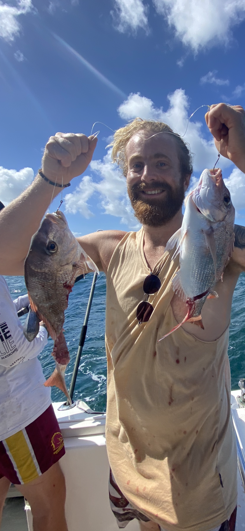 A man is holding two fish in his hands on a boat.