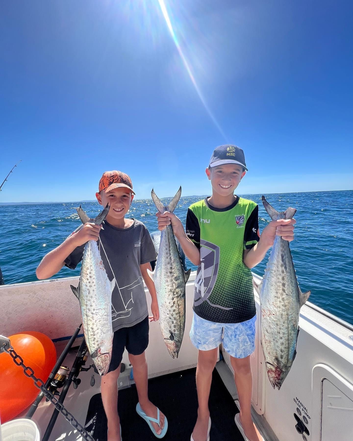 Two young boys are holding fish on a boat in the ocean.