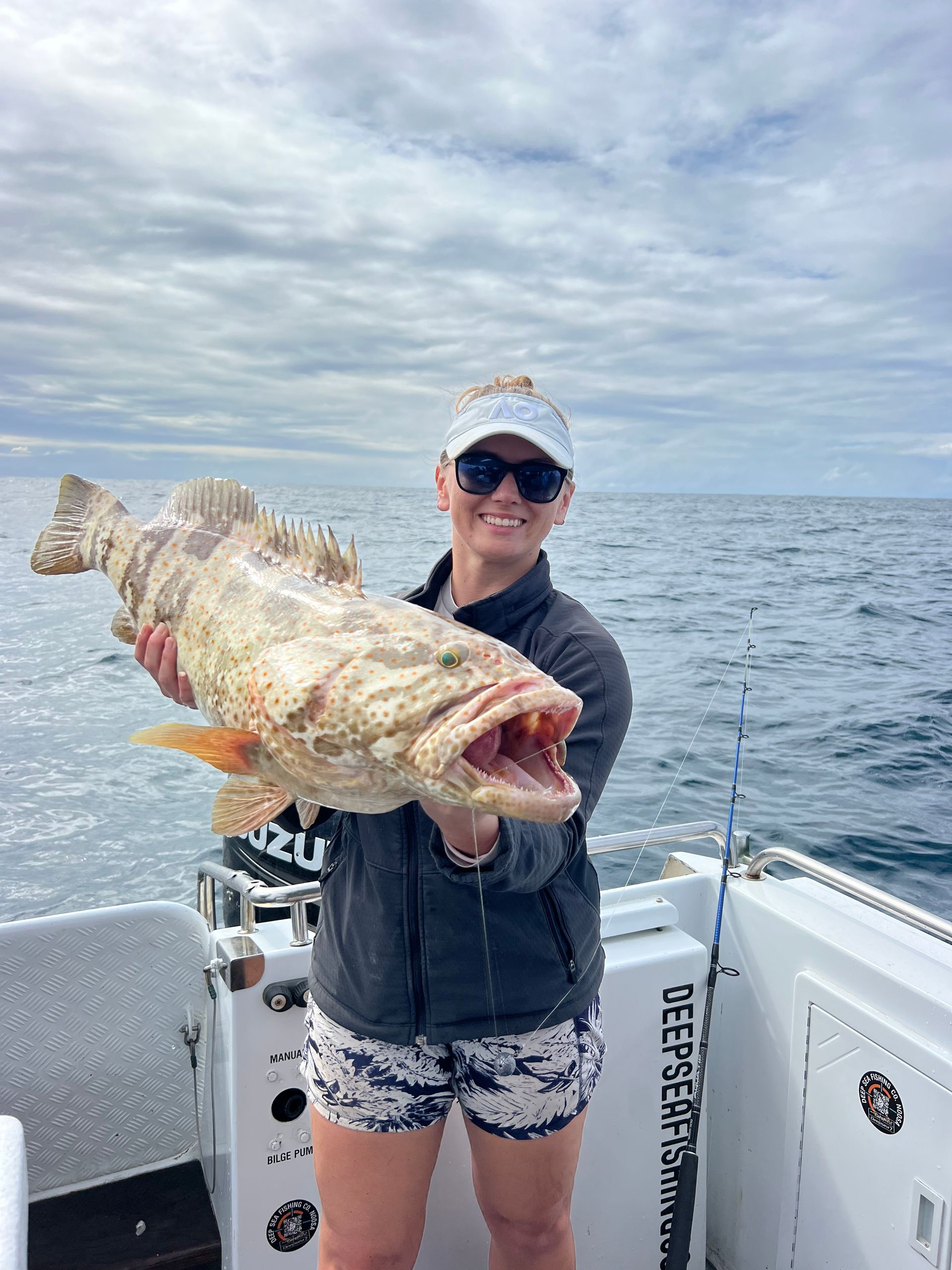 A woman is holding a large fish on a boat in the ocean.