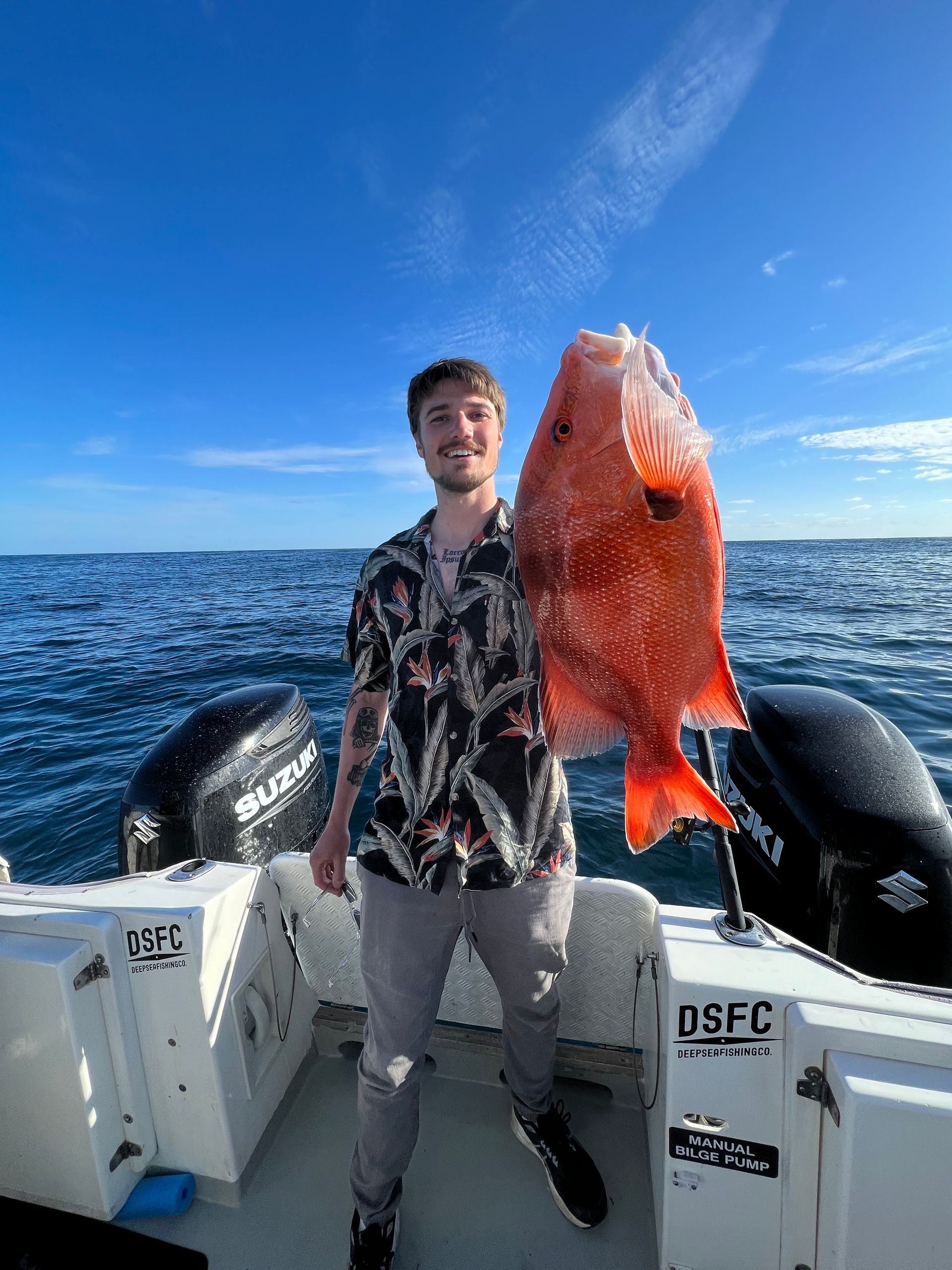 A man is standing on a boat holding a large red fish.