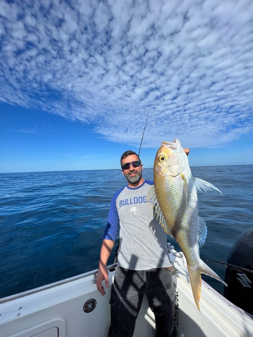 A man is standing on a boat holding a large fish.