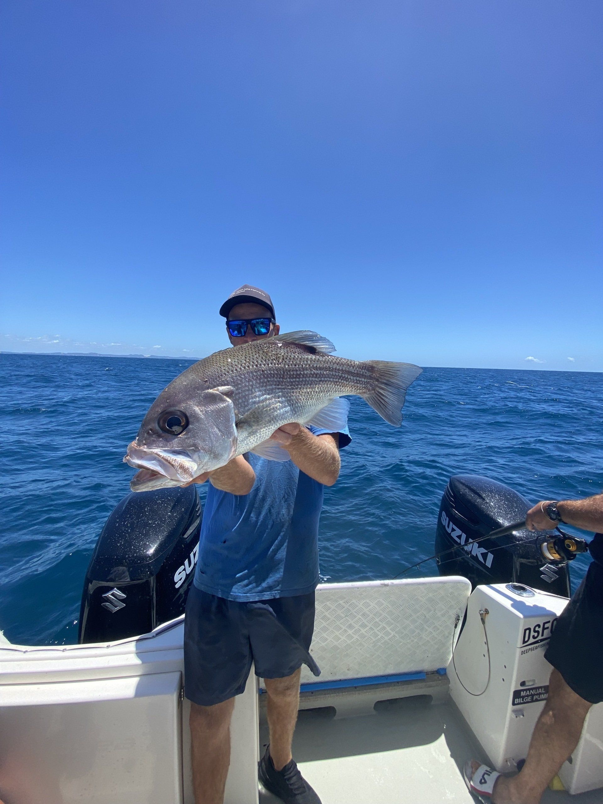 A man is holding a large fish on a boat in the ocean.