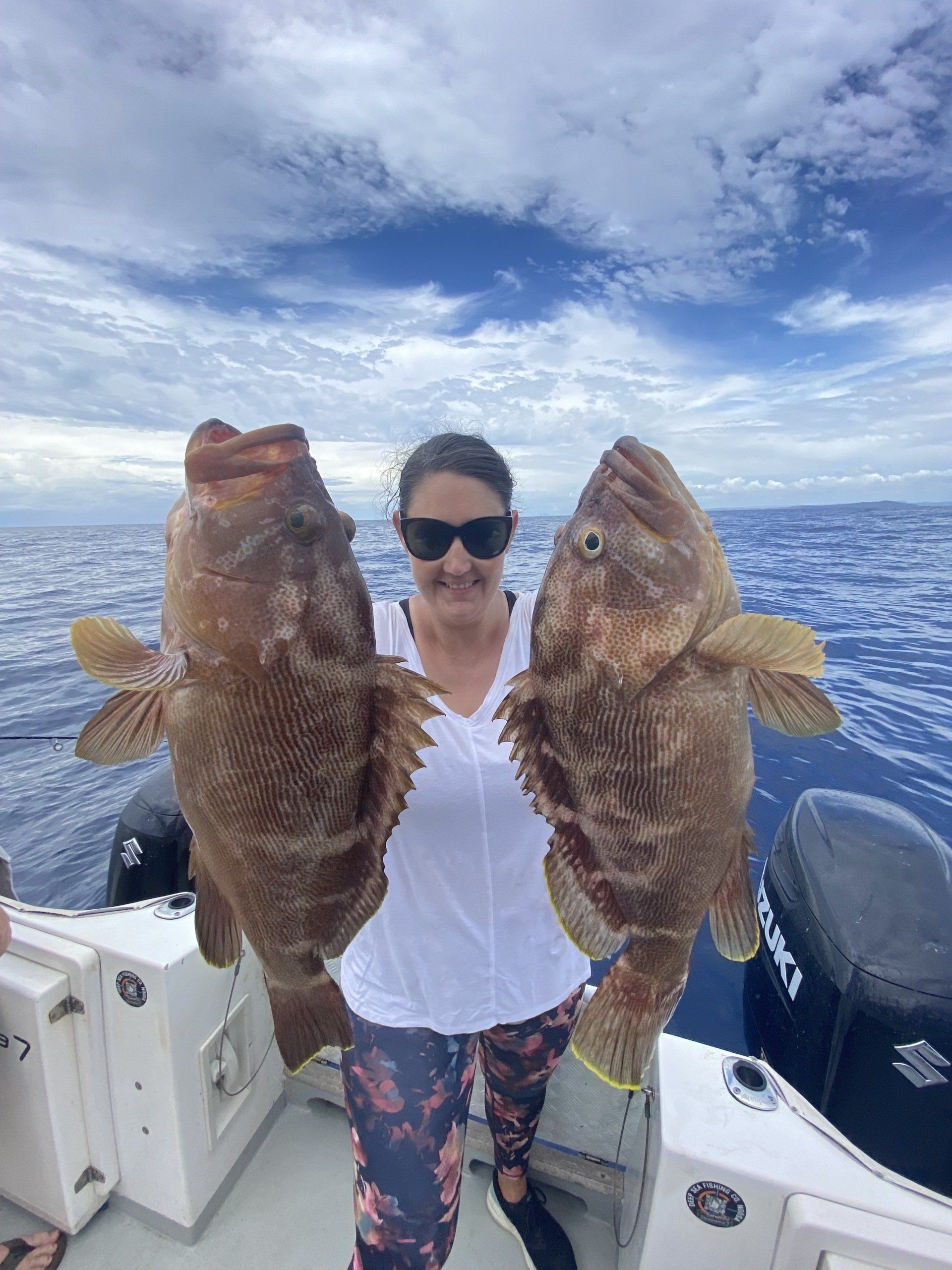 A woman is holding two large fish on a boat.