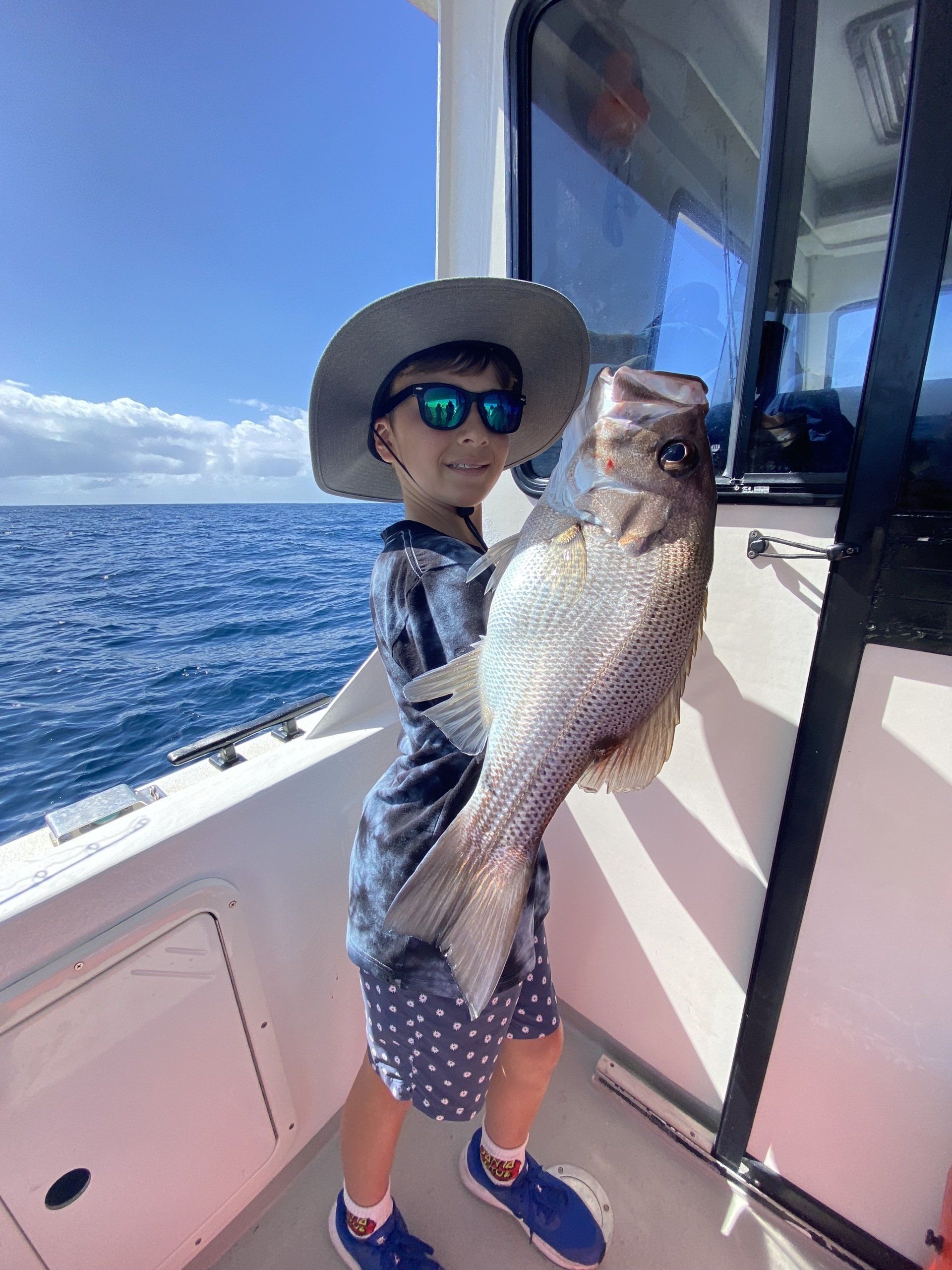 A young boy is holding a large fish on a boat.