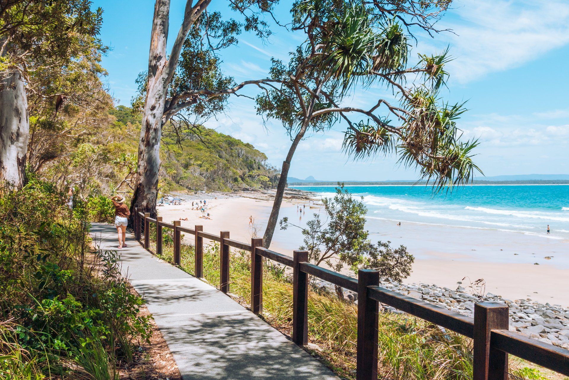 A person is walking along a path next to a beach.