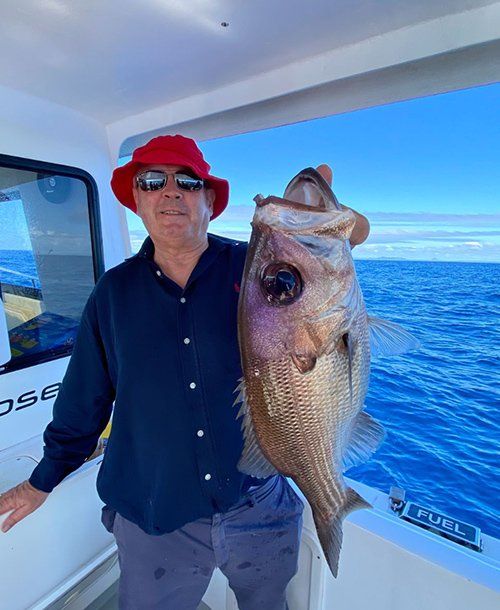 Man Wearing Red Hat Holding a Fish  Caught in Fishing Charters Sunshine Coast