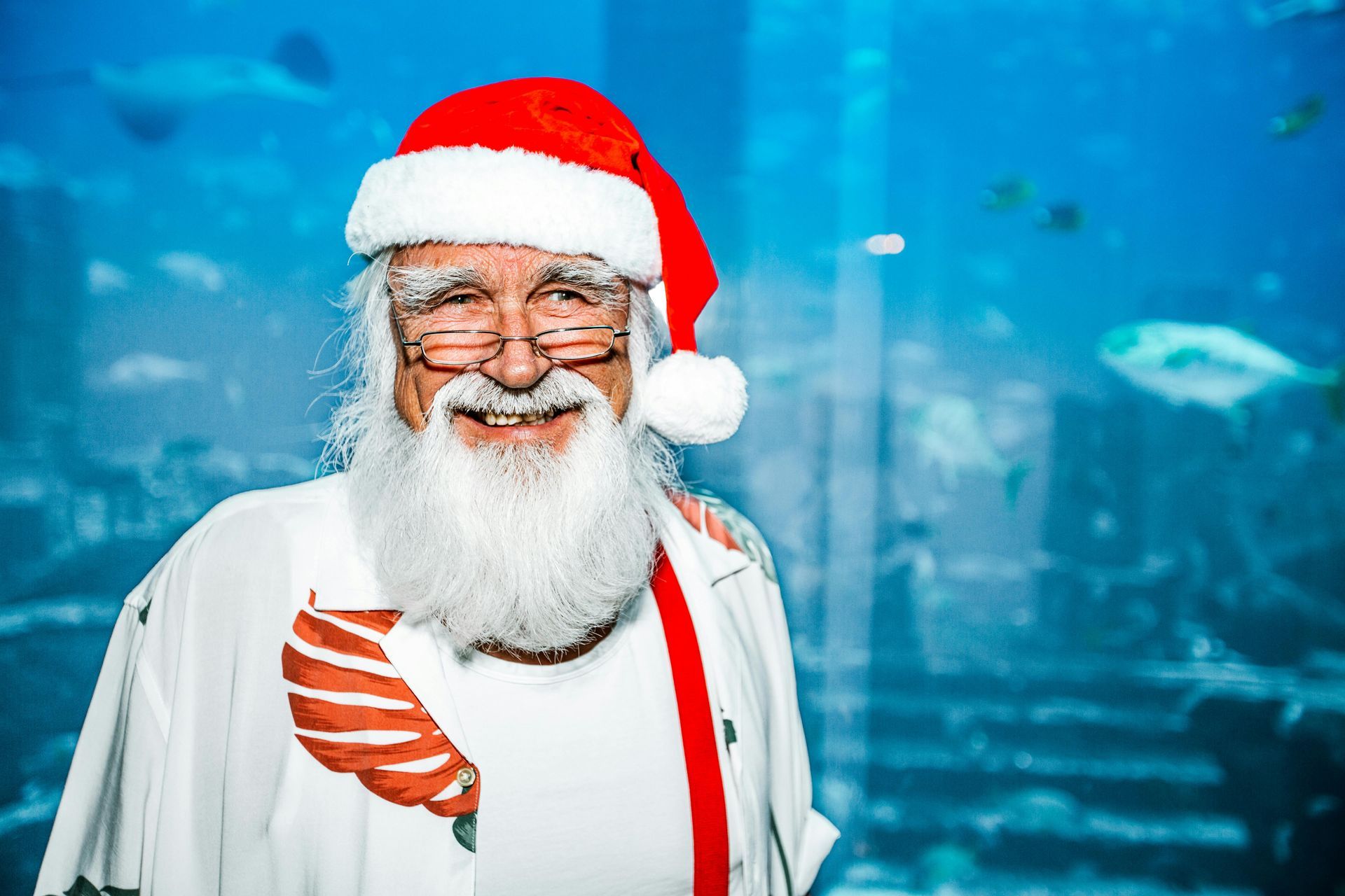 A man dressed as santa claus is standing in front of an aquarium.