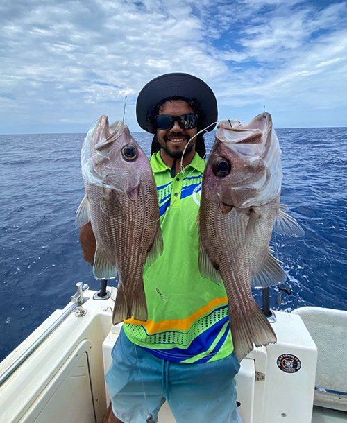 Two Freshly Caught Fish Held by a Man on the Yacht | Fishing Charters Sunshine Coast