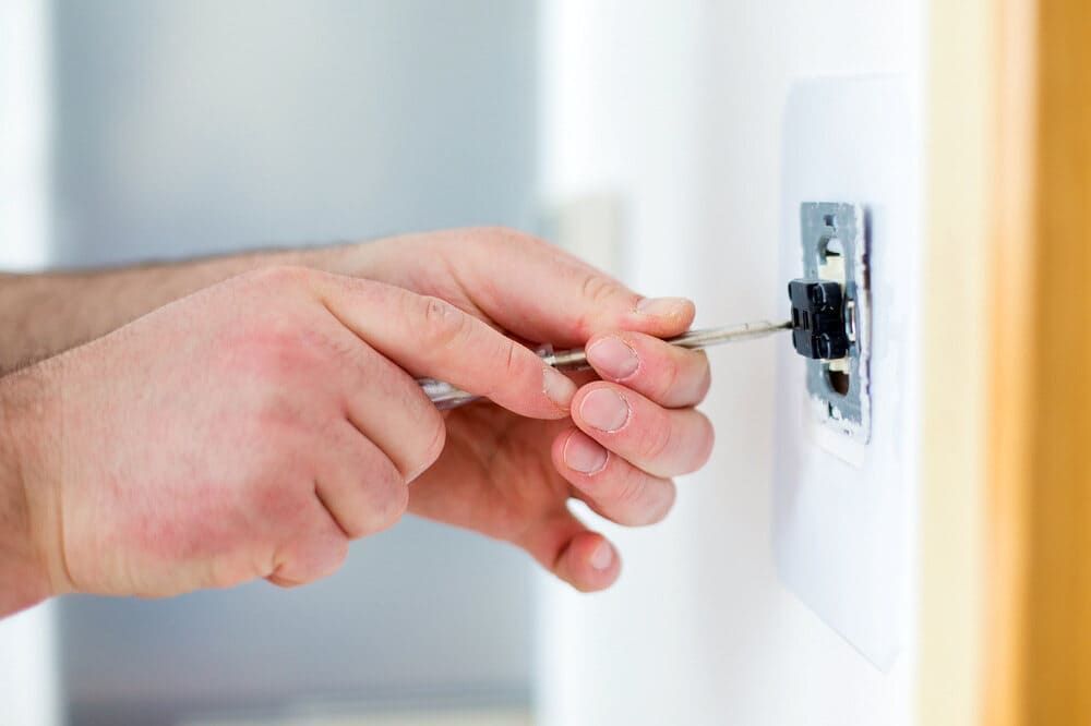 A Man is Fixing a Light Switch With a Screwdriver — Sawtell Electrical Pty Ltd In Coffs Harbour, NSW