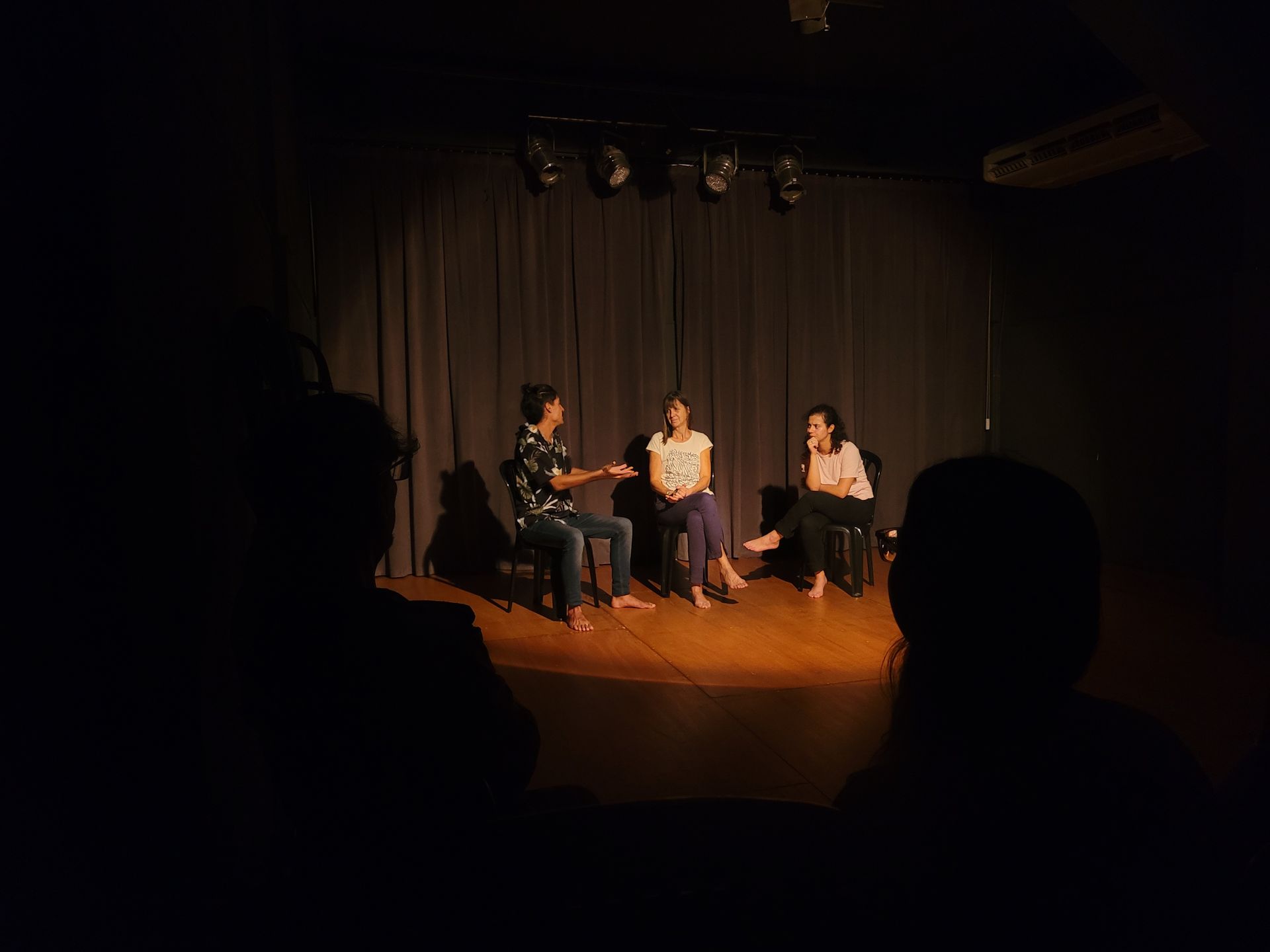 Un grupo de personas está sentado en un escenario en una habitación oscura.