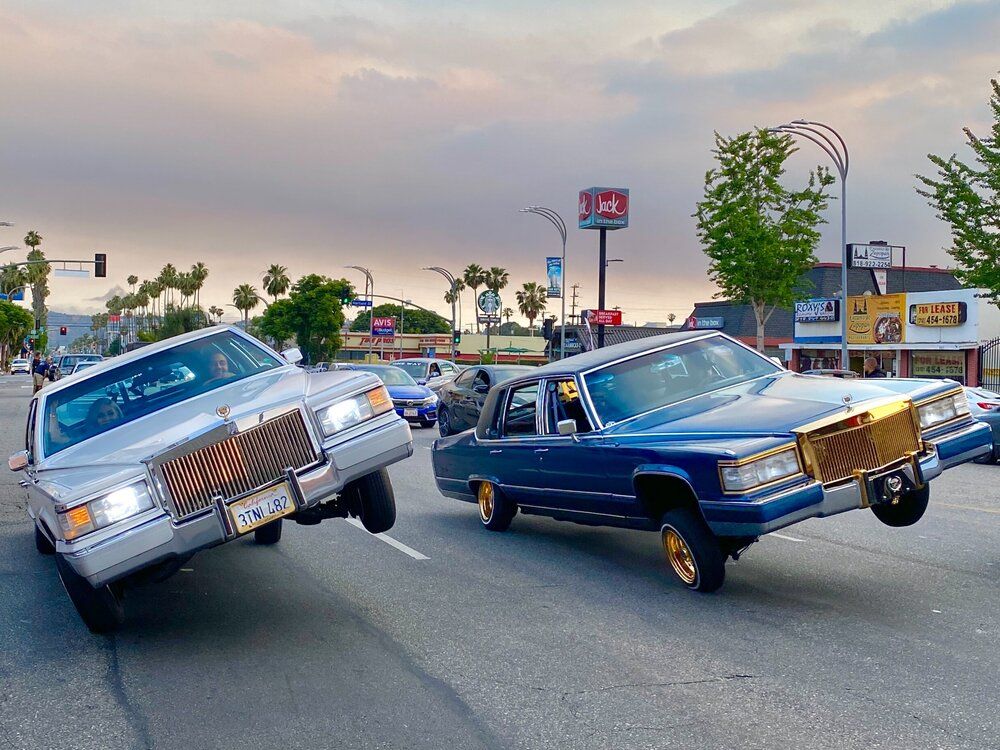 Two cars are driving down a street and one is on its side.