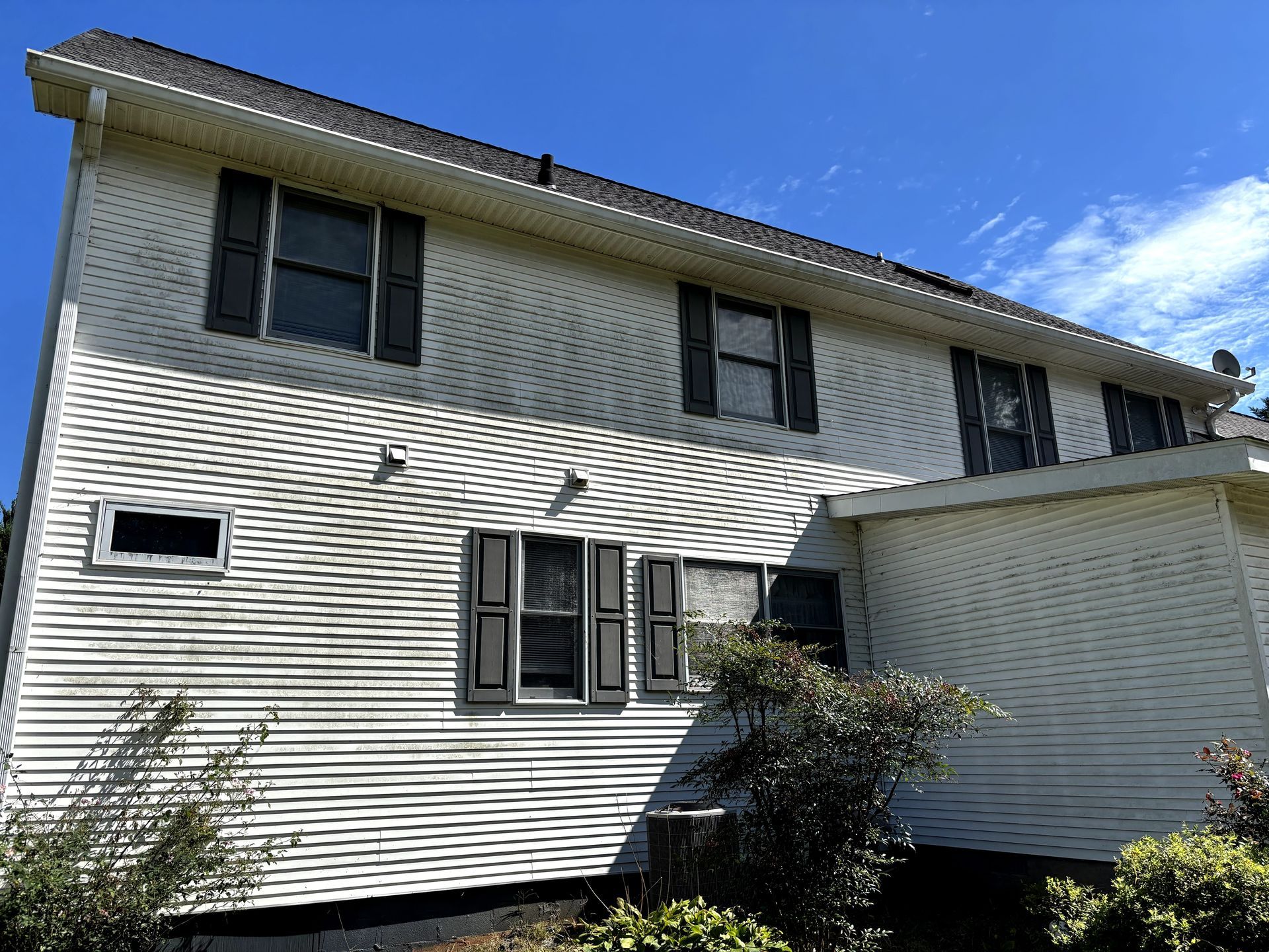 Two-story white house with black shutters under a blue sky.