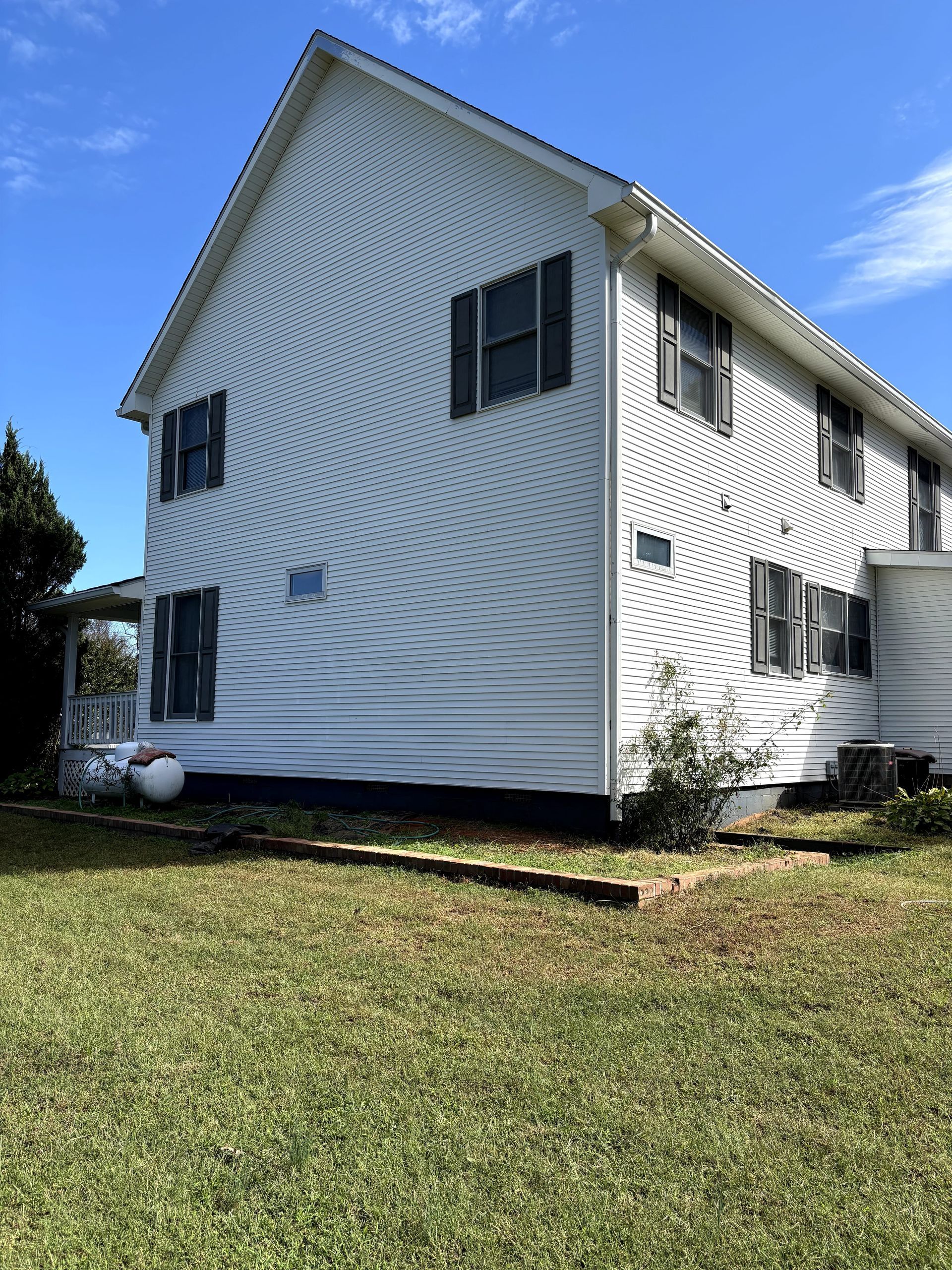 White two-story house with black shutters, set on a green grassy lawn under a blue sky.