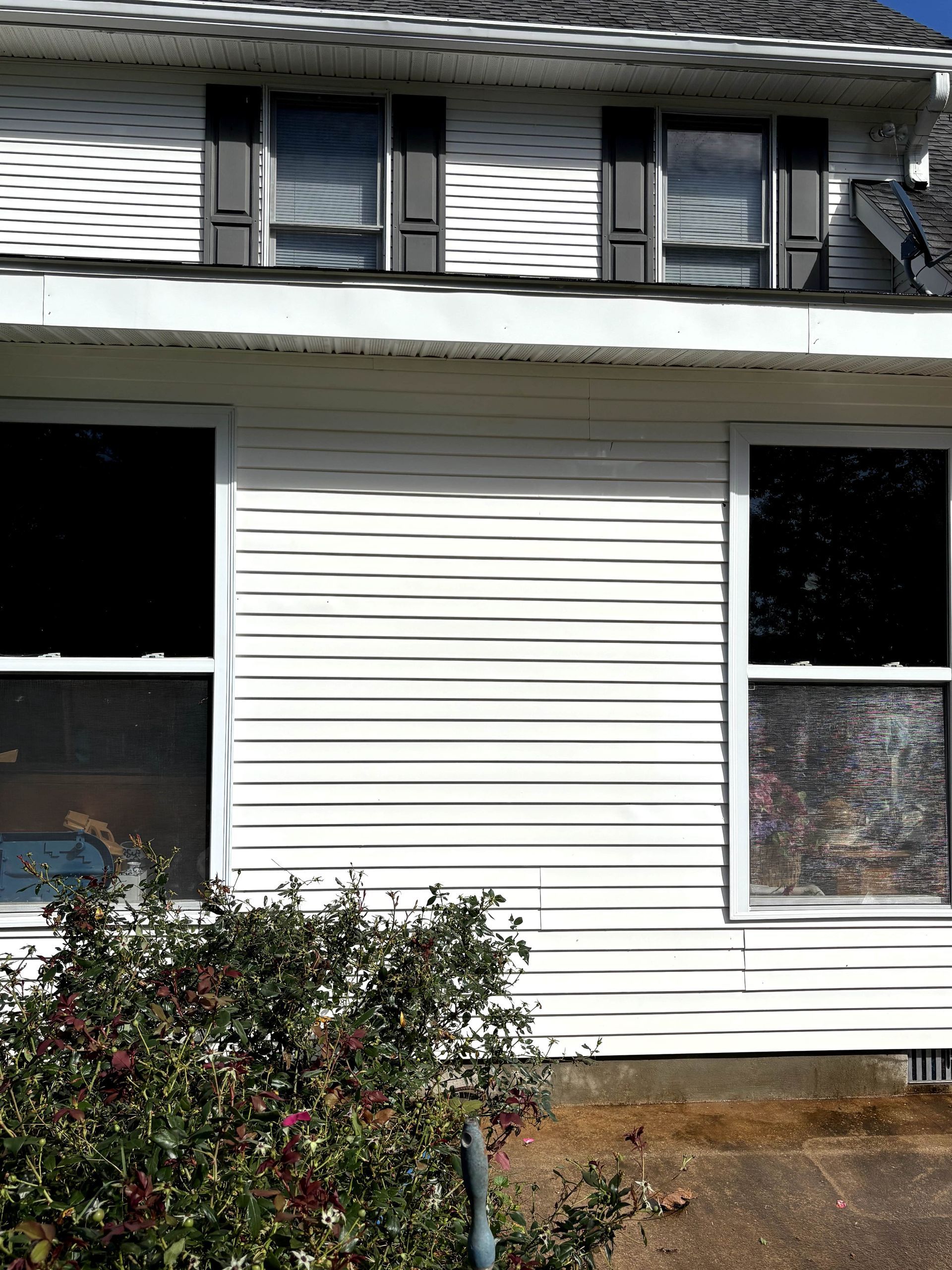 White house exterior with two upper windows, two lower windows, and gray shutters. Green bush in front.
