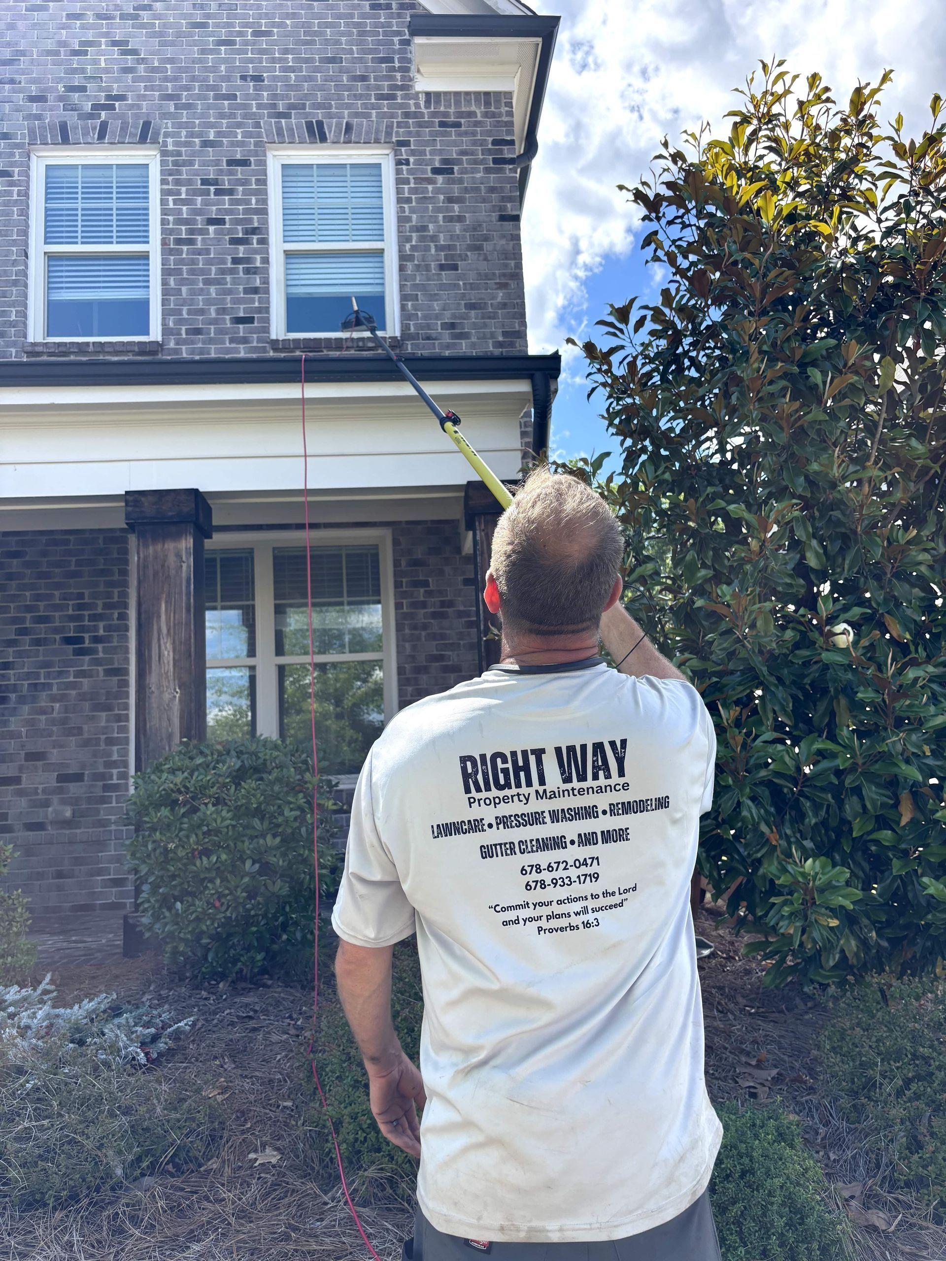 Man cleaning gutters on a house with a telescoping tool on a sunny day.