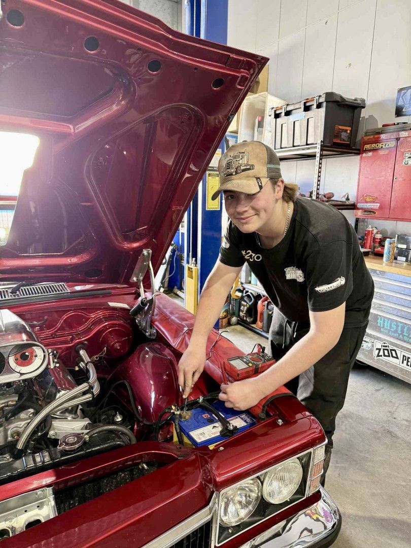 Young mechanic working on the engine of a red classic car, smiling in a garage - Gricey's Workshop Automotive Specialist in West Wodonga, VIC