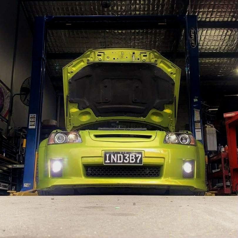 Lime green car with hood open, on a lift in a garage.