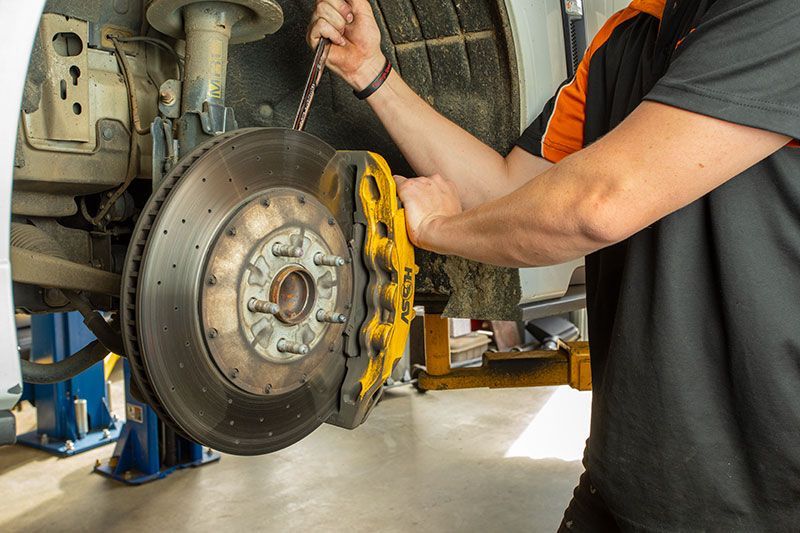 A Man is Fixing a Brake Disc on a Car in a Garage — Gricey's Workshop Automotive Specialist in West Wodonga, VIC