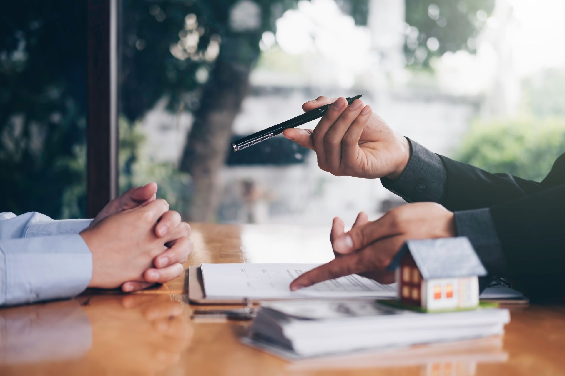 Hands signing real estate contract, small house model and cash on table.