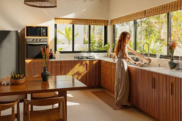 Woman washing hands at a kitchen sink with a stainless steel faucet; water running.