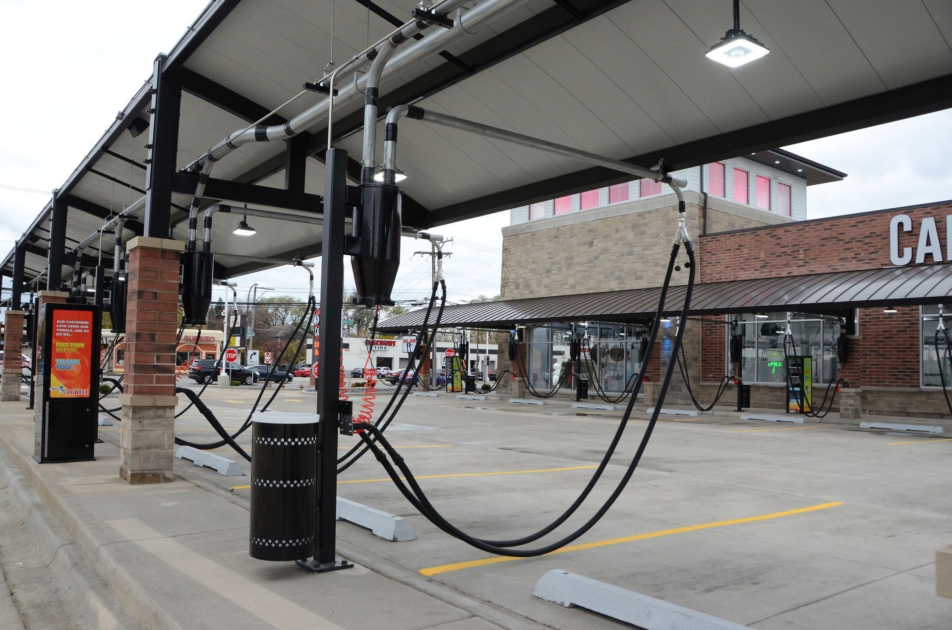 Car wash station with overhead hoses, brick columns, and a retail building.