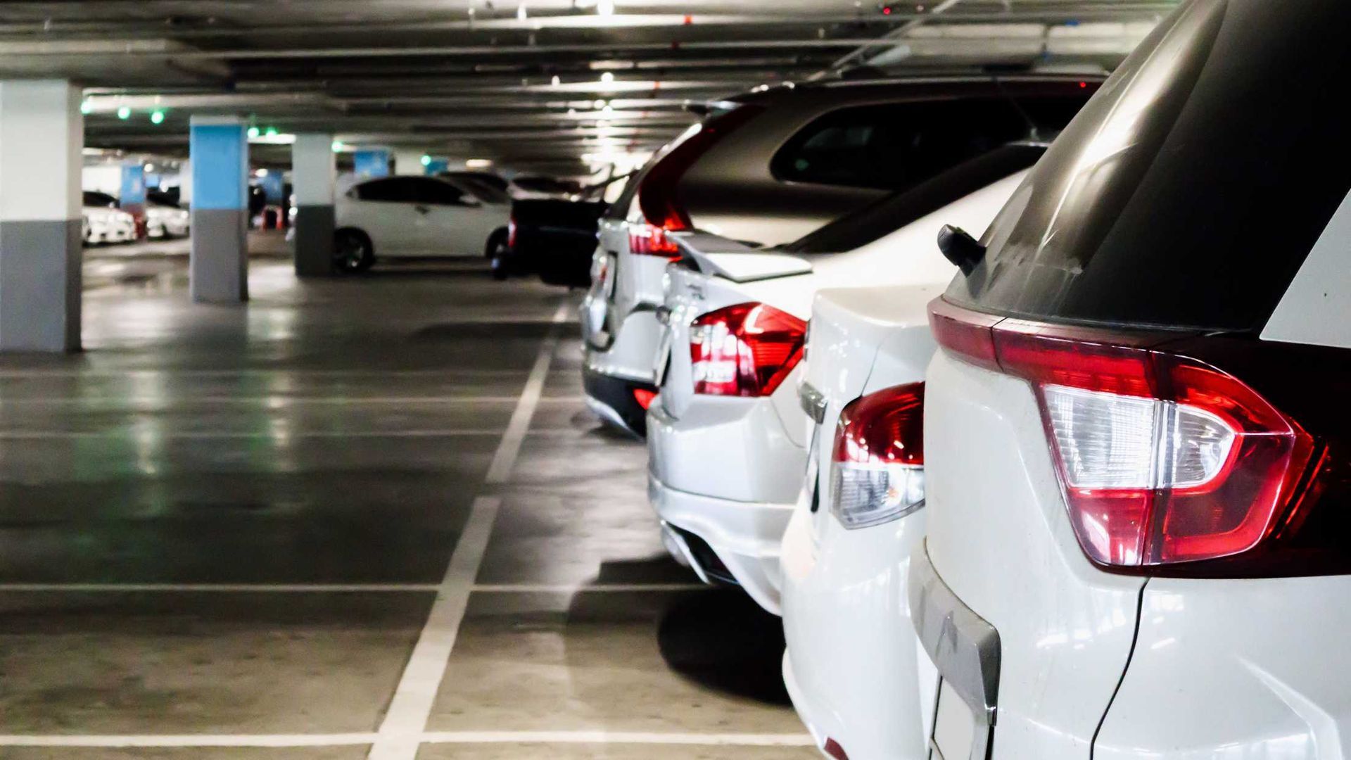 Cars parked in a well-lit underground parking garage. Several white cars are in a row.