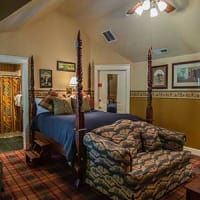 A bedroom with a four poster bed , chair , and ceiling fan.